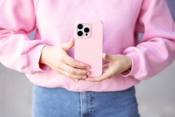 Woman holding phone in pink protective case pink sweatshirt paired with denim jeans no face. mock up with three cameras in monochrome colours back view. concept: using phone technology 