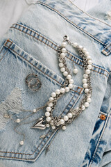 Elegant pearl and silver charm necklaces on clothes and jeans.  .Fashionable layered silver necklaces with pendants and with silver heart pendant