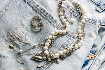 Elegant pearl and silver charm necklaces on clothes and jeans.  .Fashionable layered silver necklaces with pendants and with silver heart pendant