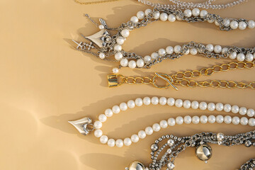 Elegant pearl and silver charm necklaces on beige background.  .Fashionable layered silver necklaces with pendants and with silver heart pendant