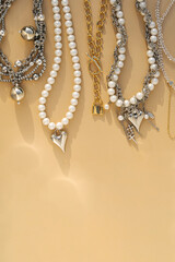 Elegant pearl and silver charm necklaces on beige background.  .Fashionable layered silver necklaces with pendants and with silver heart pendant