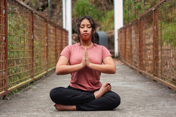 Young woman practicing yoga and meditating on a bridge