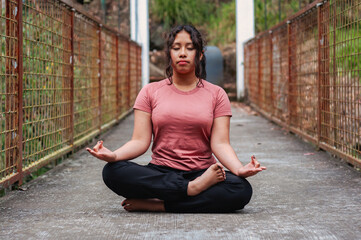 Young hispanic woman meditating outdoors on a bridge