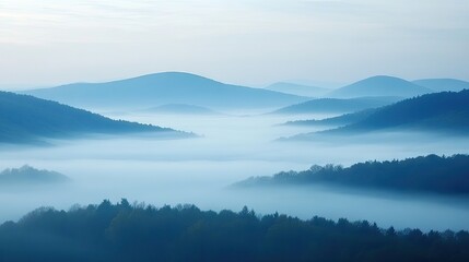 Fototapeta premium Fog rolling over forested mountains at sunrise creating a serene, misty landscape