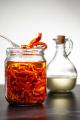 Sun dried tomatoes with herbs and olive oil in jar. Dried tomatoes with herbs and olive oil on a black table and white background. Shallow depth of field