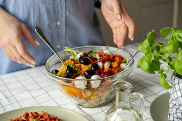 Women cooking salad with tomato tomato mozzarella vegetables and arugula in a large bowl 