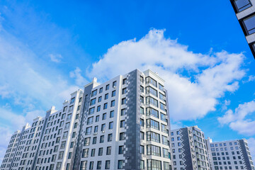 Fototapeta premium The concept of a multi-storey lady, a residential complex. A view from below of the houses of the residential complex, which stand one after the other three houses, houses of modern architecture with