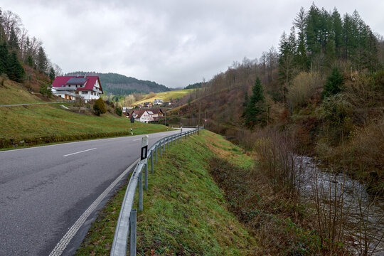 Scenic Mountain Road with Traditional Houses and Red Roofs in Black Forest Valley Landscape. Winding Rural Highway Through Alpine Village with White Buildings and Green Forest Hills Under Cloudy Sky. - Powered by Adobe