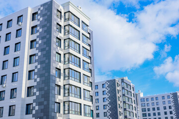 Fototapeta premium The concept of a multi-storey lady, a residential complex. A view from below of the houses of the residential complex, which stand one after the other three houses, houses of modern architecture with