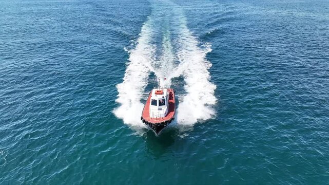 Aerial drone cinematic tracking video of red pilot boat cruising in high speed in Mediterranean deep blue sea offering navigational aid to ships