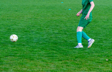 a football player in a green football uniform runs up to a flying ball on the pitch. green grass on a football pitch.