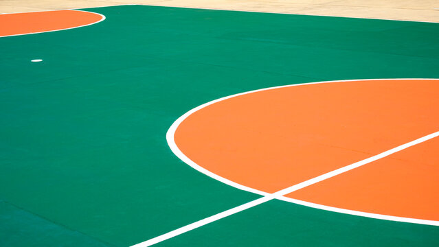 Outdoor futsal court background with orange circle center pattern and white outline on green concrete floor surface, sport field backdrop