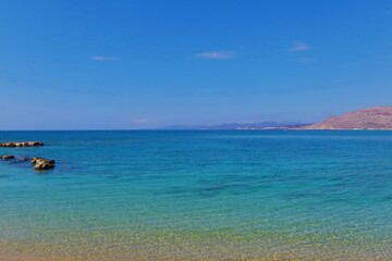 Obraz premium Beautiful beach, calm turquoise sea surface and distatn horizon. Calm ocean, distant orange sandy shore. Travel photography from the shoreline. Day on the beach, vacation photo.
