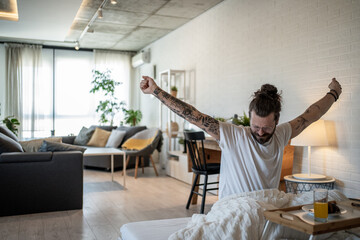Fototapeta premium Tattooed freelancer waking up and stretching in bed at home