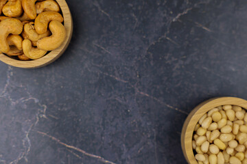 Delicately arranged cashew and pine nuts sit beautifully in wooden bowls against a stunning dark...