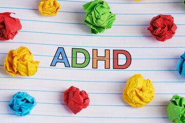 ADHD. The abbreviation ADHD written on a notebook sheet with some colorful crumpled paper balls...