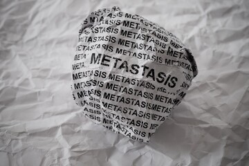 Crumpled paper ball with words Metastasis on a crumpled white paper background.