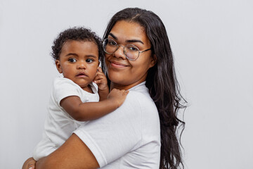 Beautiful Brazilian mother hugs and kisses her baby in the studio on a white background. A young...