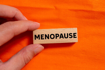 Menopause message written on wooden block on orange background. Conceptual menopause symbol. Copy space.