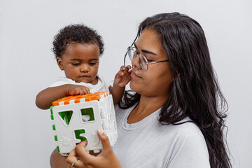 Beautiful Brazilian mother hugs and kisses her baby in the studio on a white background. A young mother in a white bodysuit hugs and plays with her baby in the studio. Black baby, African baby. Brazil