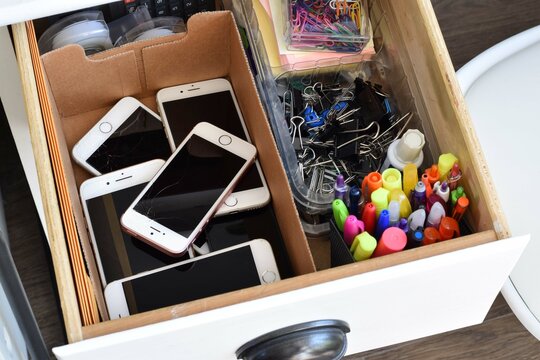 A collection of old broken outdated iPhones inside a junk drawer, illustrating technology waste