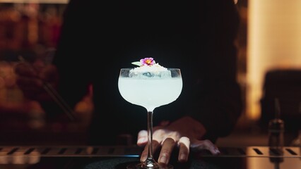 Bartender serving mixed creamy vodka cocktail glass adding pink flower top with sugar burned on ice at bar, focusing alcohol refreshing special created menu at luxurious counter nightclub. Vinosity.