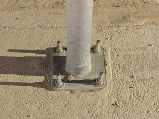 Close-up of a metal pole base anchored to a concrete surface with bolts and a metal plate.