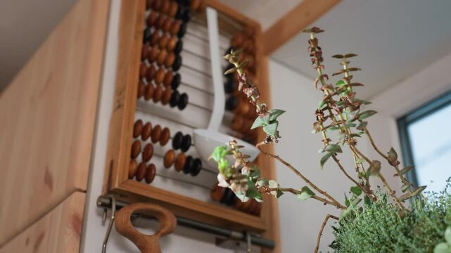 Green potted plant placed near hanging kitchen utensils including wooden cutting board and ladle, with vintage wooden abacus in background