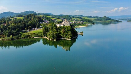 Obraz premium Aerial view of Niedzica Castle in Poland. The castle perched on a hill surrounded by lush greenery and a serene lake. The medieval structure features stone walls and towers