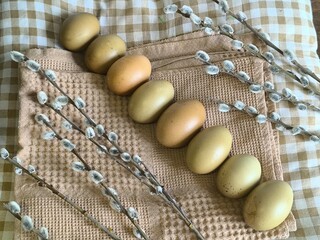 easter eggs lie diagonally in a row on a beige towel on a checkered tablecloth and willow branches