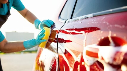 Hands in protective gloves washing red car with yellow sponge and foam, close up, auto care, vehicle cleaning, detailing service, maintenance, blog tutorial, car wash promotion