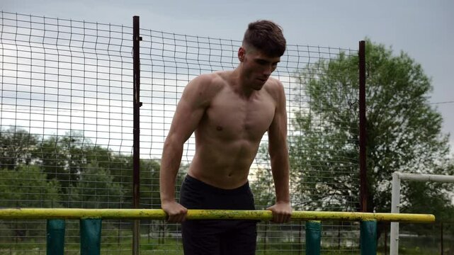 Male shirtless athlete doing push ups on parallel bars at nature. Strong sporty man exercising at sports ground. Young sportsman training hard outdoor. Concept of active sportive lifestyle. Slow mo