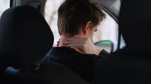 Driver stretches his tired neck while sitting in the car, rear view