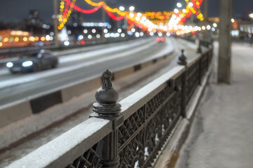 A cast-iron fence by the road with a view of multi-colored garlands above the roadway.