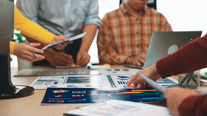 A diverse group of professionals collaborates in a modern office setting, analyzing data charts and graphs to develop effective business strategies through teamwork. SACTR