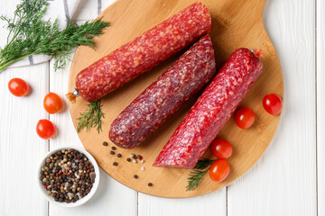 Different smoked sausages, cherry tomatoes and spices on white wooden table, flat lay