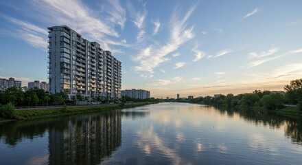 Fototapeta premium Modern Waterfront Apartments at Sunset - Stunning view of modern apartment buildings along a calm river at sunset, reflecting the sky and clouds