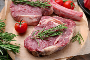 Pieces of raw beef, rosemary and tomatoes on table, closeup