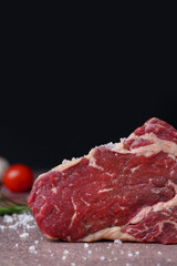 One piece of raw beef with salt on brown textured table against black background, closeup. Space for text
