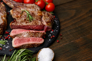 Pieces of delicious beef meat, spices and tomatoes on wooden table, closeup. Space for text