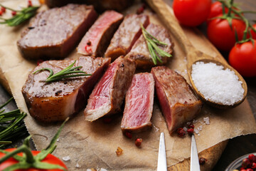 Pieces of delicious beef meat, spices and tomatoes on table, closeup