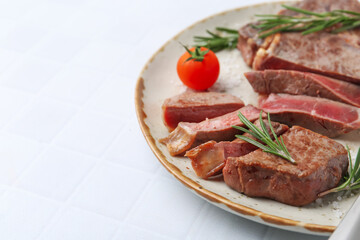 Pieces of delicious beef meat, spices and tomato on white tiled table, closeup. Space for text