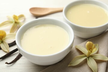 Tasty condensed milk, vanilla pods, flowers and spoon on white wooden table, closeup
