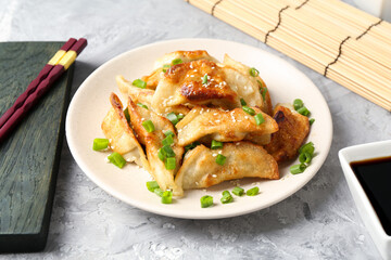Tasty fried gyoza (dumplings), soy sauce and chopsticks on light grey table