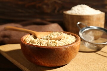 Brown rice, flour and sieve on wooden table, closeup