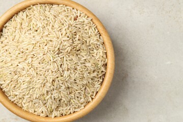 Brown rice in bowl on light grey table, top view. Space for text