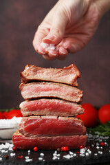 Woman salting delicious sliced beef tenderloin with different degrees of doneness at table against brown background, closeup