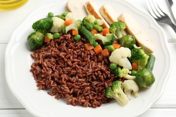 Tasty brown rice with vegetables and chicken on white wooden table, closeup
