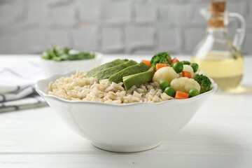 Tasty brown rice with vegetables in bowl on white wooden table, closeup