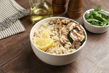 Delicious brown rice with mushrooms, zucchini and lemon slices served on wooden table, closeup